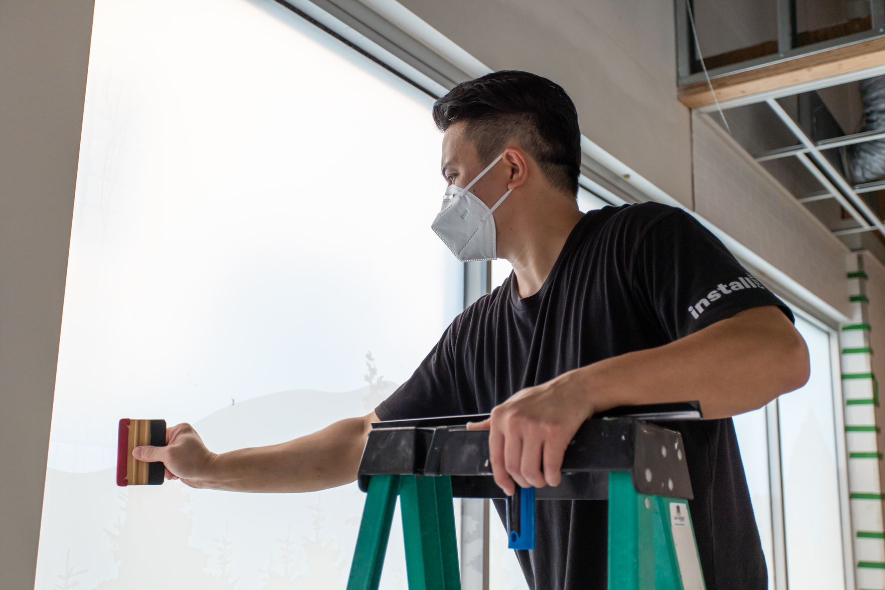 Can-Design installer applying frosted window film on commercial glass interior.