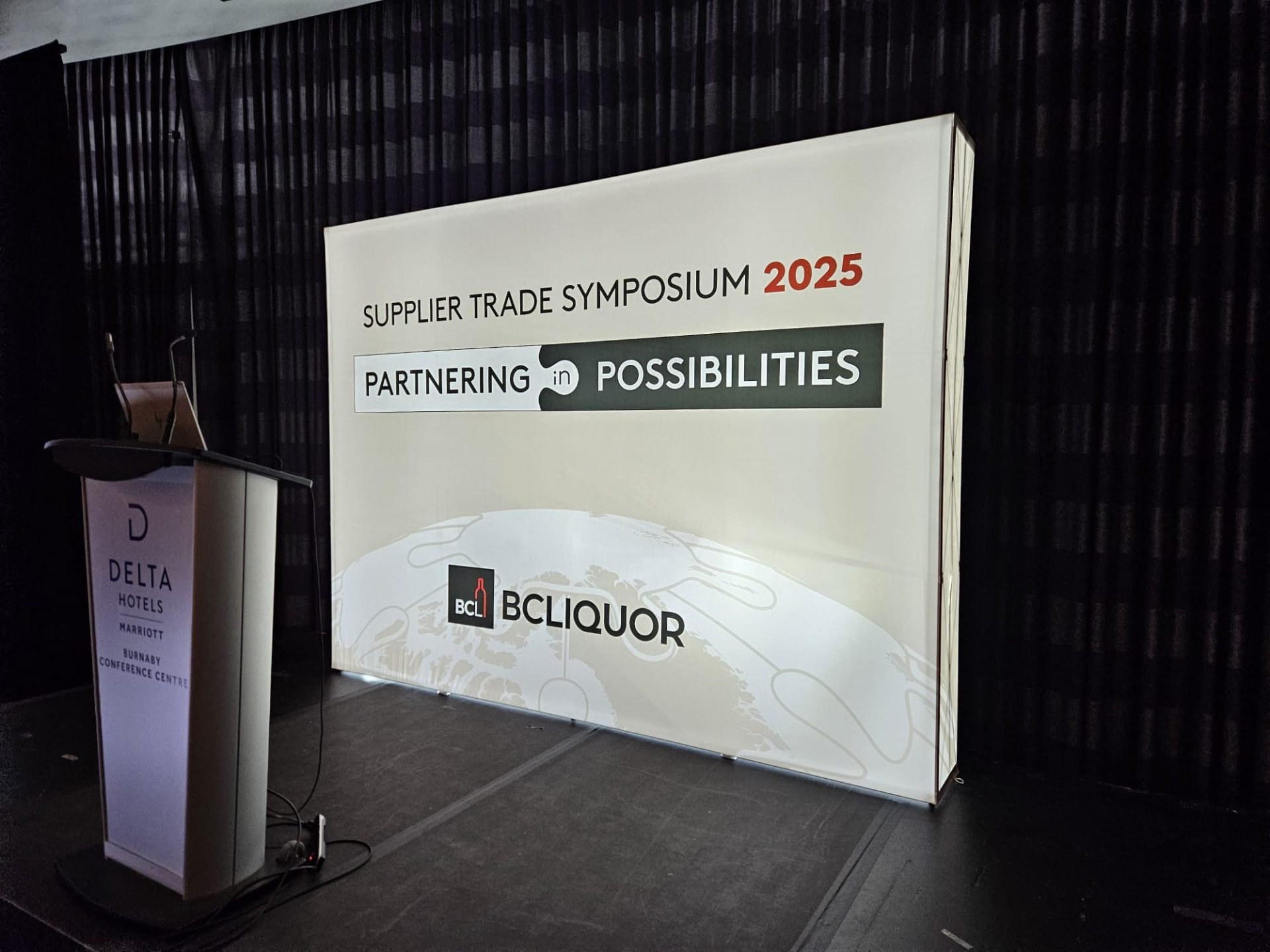 Stage backdrop for BC Liquor Supplier Trade Symposium 2025 at Delta Hotels Burnaby Conference Centre, featuring branded event signage and podium.
