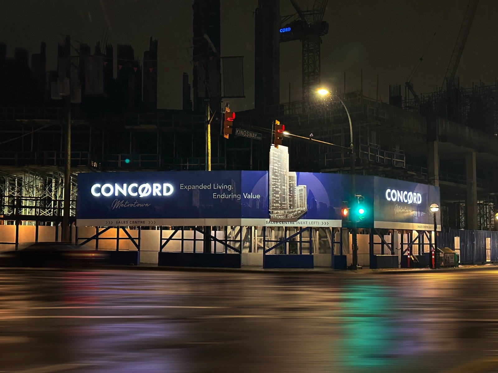Construction sight at night with illuminated Concord hoarding signage promoting real estate development on Kingsway