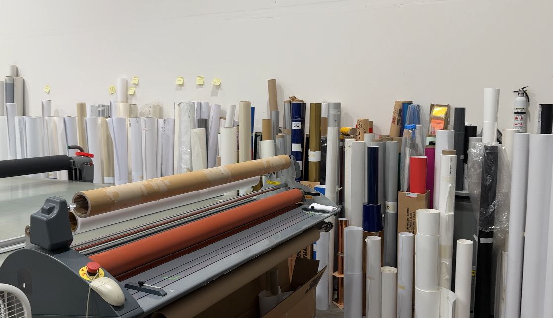 Vinyl rolls and large-format printing equipment in a signage workshop, used for creating window graphics, wall wraps, and outdoor promotional signage.